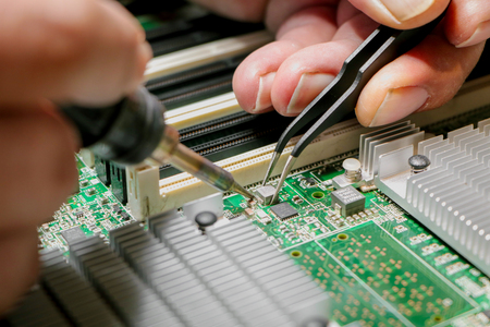 Hand with a soldering iron over a circuit board
